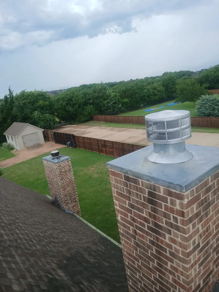 Brick chimney with a metal cap on a residential roof overlooking a large backyard.