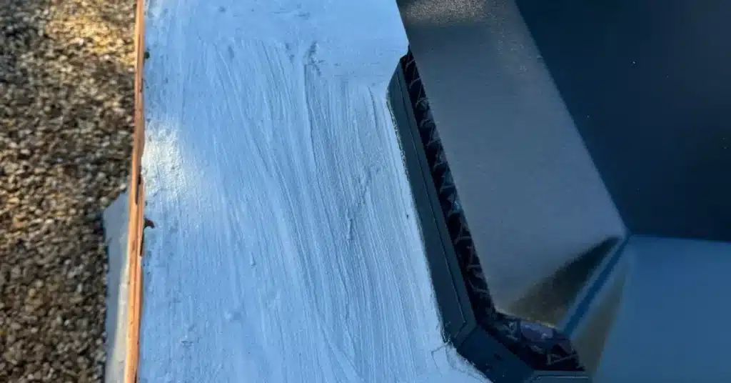 Wet sealant applied around metal chimney flashing on a roof, showing fresh coating by Chimney Professionals.