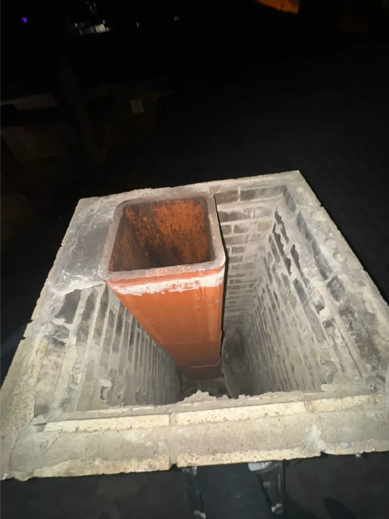 Brick chimney shaft with an orange flue liner extending downward, showing the interior area above the chimney damper.