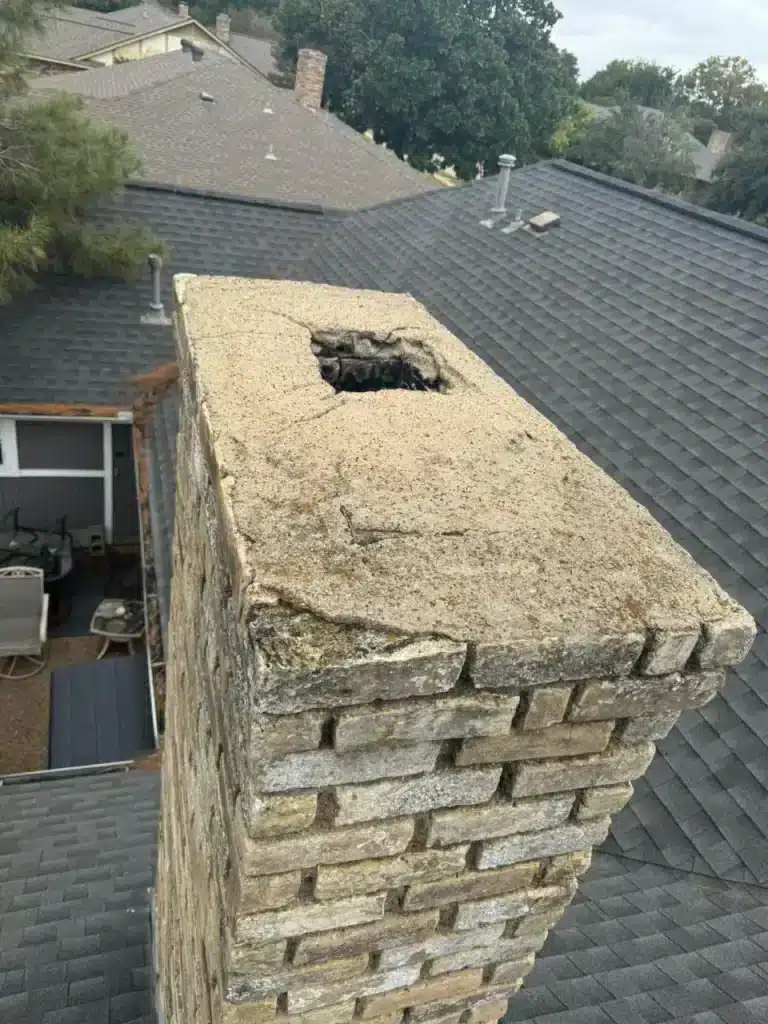 Damaged brick chimney top with cracked crown and open flue inspected by chimney sweepers on a residential roof.