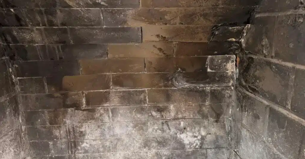 Soot-stained and cracked firebox walls showing heat damage and residue buildup inspected by chimney sweepers.