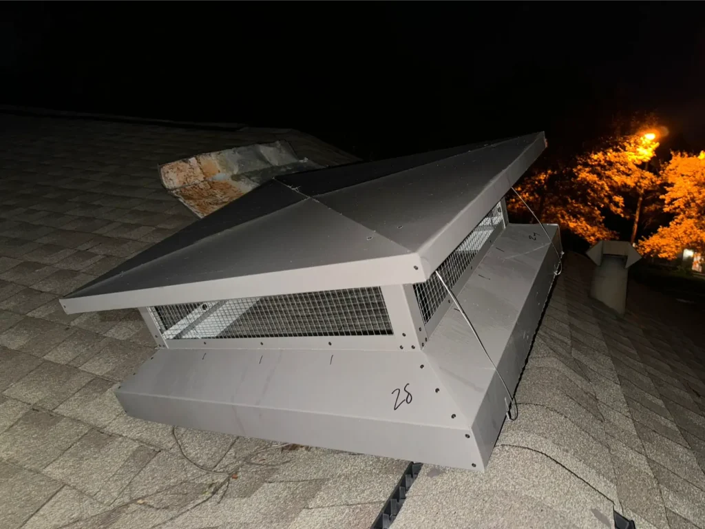 Metal rooftop chimney cap installed above faux fireplace flue at night.