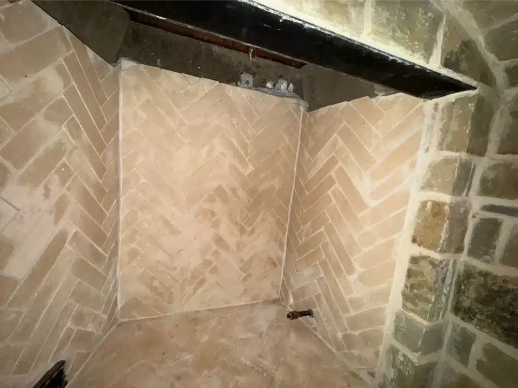 Clean herringbone firebox with exposed gas stub as part of a faux fireplace rebuild.
