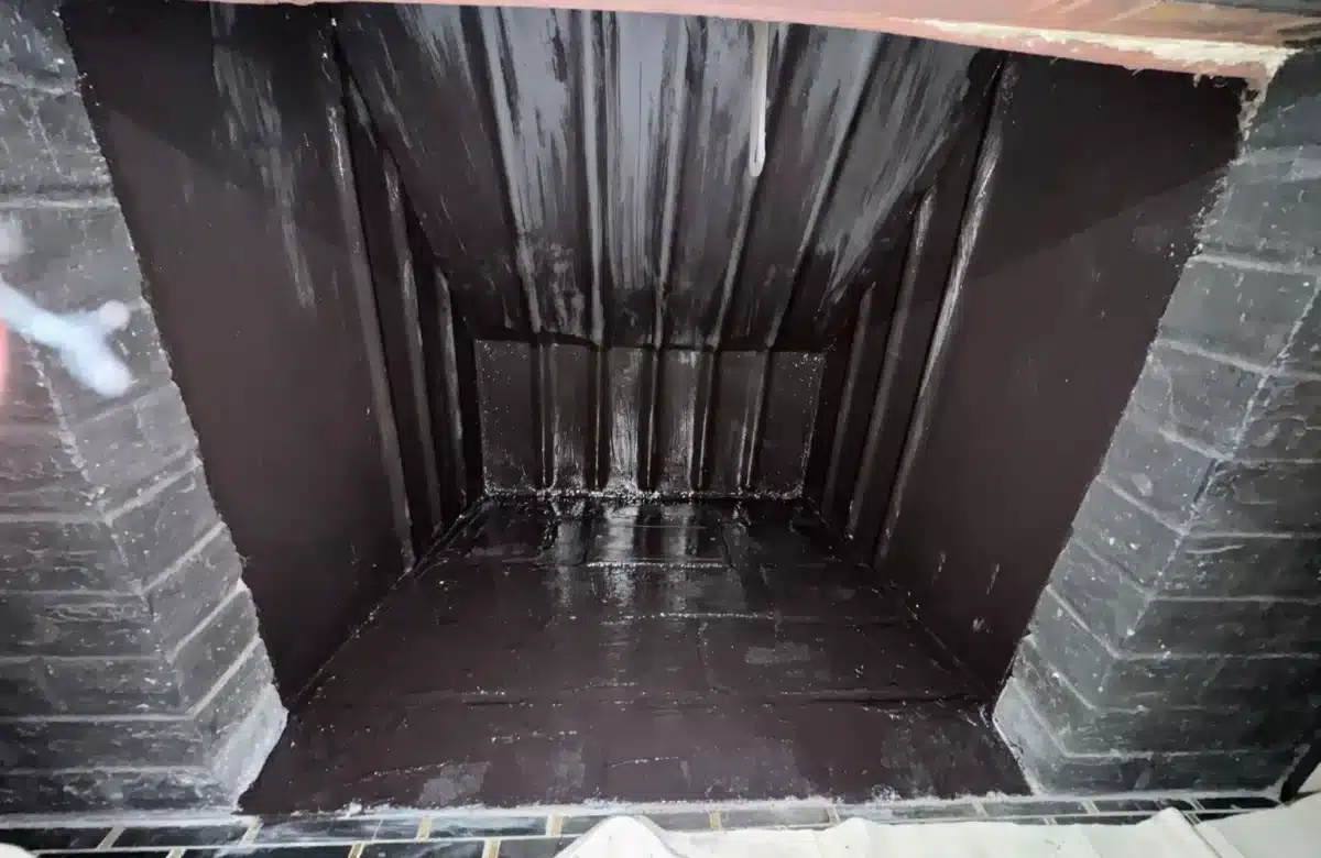Freshly coated black fireplace firebox interior after chimney damper and firebox restoration work.