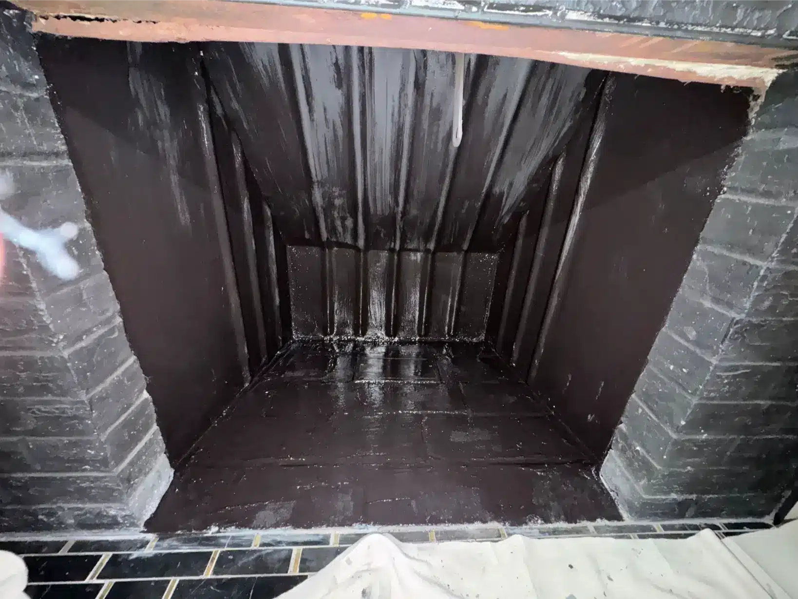 Freshly coated black fireplace firebox interior after chimney damper and firebox restoration work.