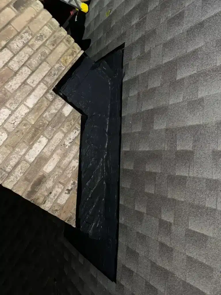 Roofline detail showing black flashing and shingle transition against brick chimney, relevant to fireplace code compliance.