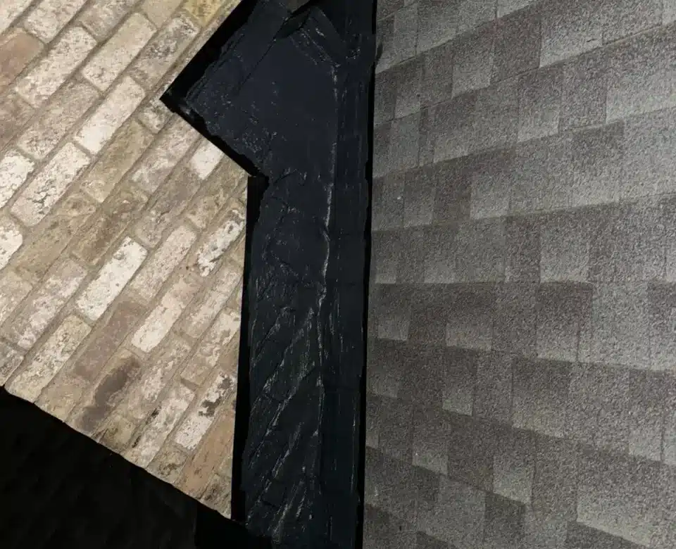 Roofline detail showing black flashing and shingle transition against brick chimney, relevant to fireplace code compliance.