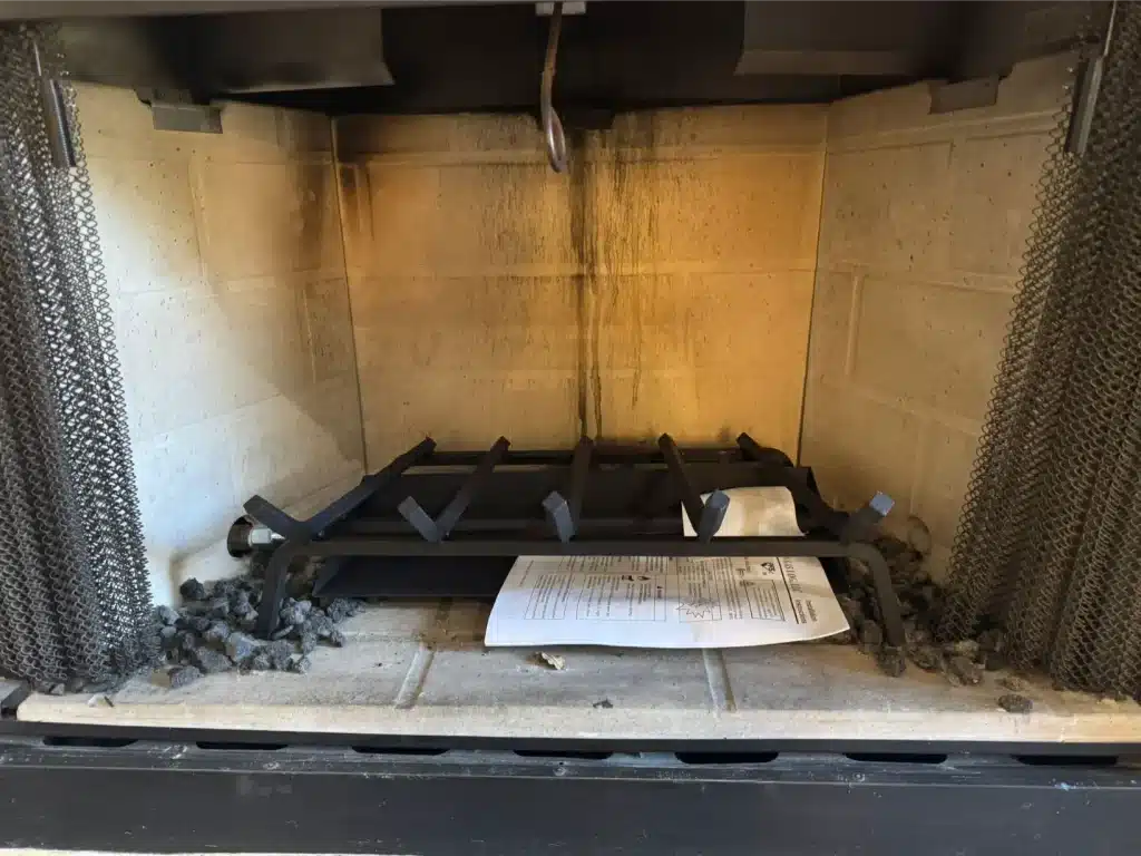 Fireplace interior with soot-stained firebox and metal grate, highlighting potential fireplace safety concerns.