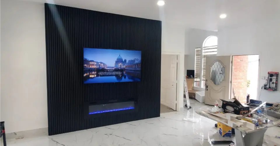 Modern living room with black slat accent wall featuring mounted TV and electric fireplace under bright recessed lighting.