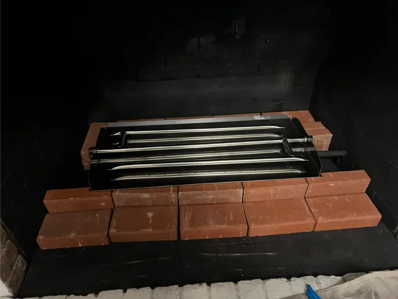New gas fireplace installation with red fire bricks and stainless steel burner tray in a black firebox.