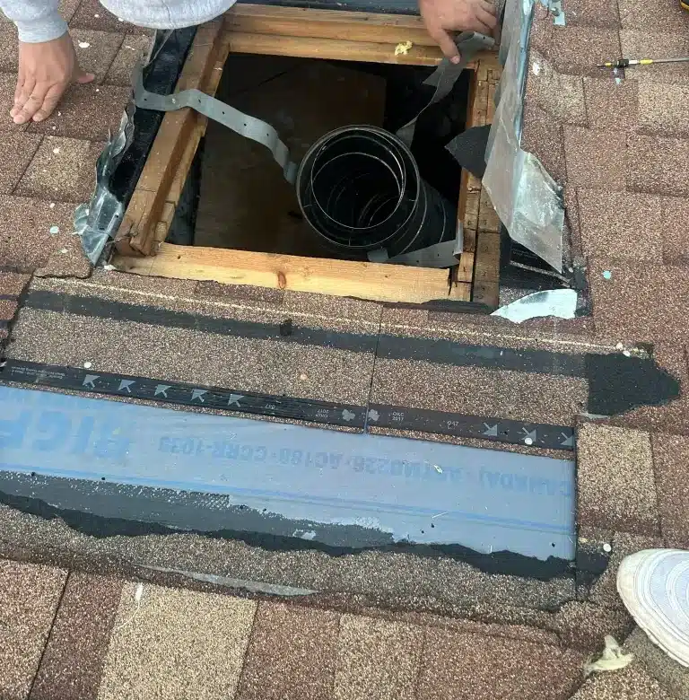 Worker repairing roof opening with exposed framing and vent pipe surrounded by shingles and flashing