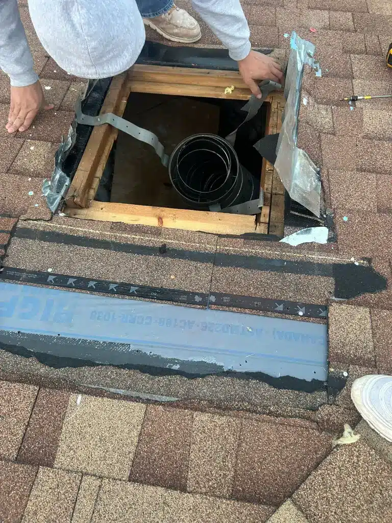 Worker repairing roof opening with exposed framing and vent pipe surrounded by shingles and flashing
